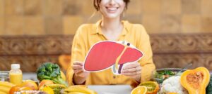 Uśmiechnięta kobieta trzyma w ręku rysunek wątroby. Wątroba a młodość